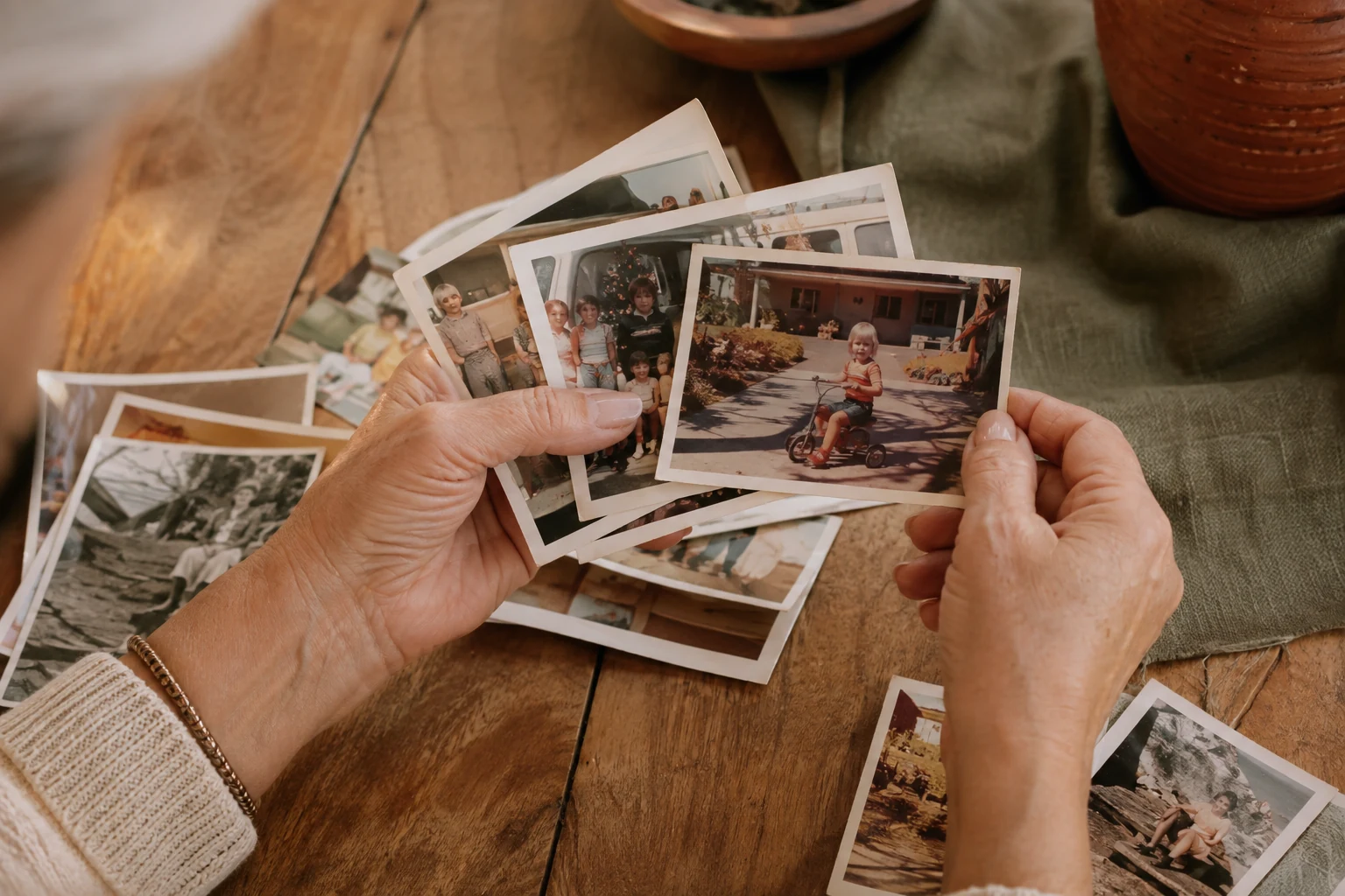 Hands gently sorting vintage family photographs on a sunlit wooden table